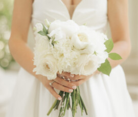 Close-up of bride holding a bouquet of white roses and peonies while wearing a pearl necklace and strapless gown.