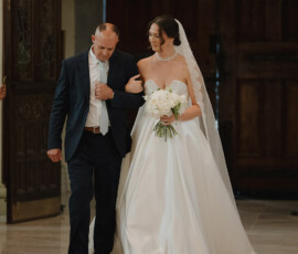 Bride in white gown and veil walks with suited man down Cathedral-Basilica aisle at classic Mobile Alabama wedding.