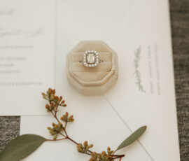 Diamond ring in velvet box on envelope, green leaves, and invitation evoke timeless Mobile Alabama wedding elegance.
