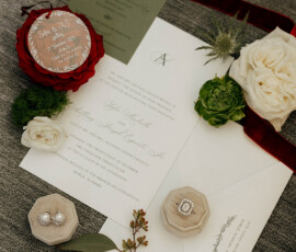 Wedding invitations, envelopes, greenery, a rose, ring boxes, and keepsake on a grey surface—ideal Mobile wedding inspiration.