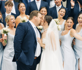 Wedding party cheering as the bride and groom kiss during a joyful group portrait outside the church.