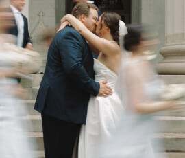 Bride and groom kiss on stone steps, surrounded by guests in blue at their joyful Cathedral-Basilica Mobile wedding.