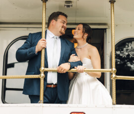 Bride and groom in wedding attire smile on a white trolley with gold railings at their Battle House Mobile wedding.