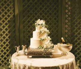 Three-tier white wedding cake with flowers on a lace table, surrounded by decor at an elegant Mobile Alabama wedding.