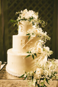 Three-tier white wedding cake decorated with cascading fresh white flowers and monogram initials
