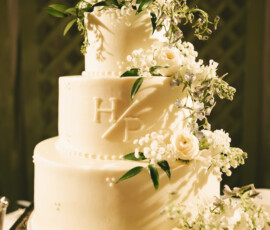 Three-tier white wedding cake decorated with cascading fresh white flowers and monogram initials