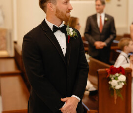 Man in black tuxedo stands in church with pews and stained glass behind him at a classic Mobile Alabama wedding.