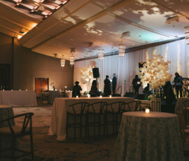 Elegant Battle House wedding venue in Mobile, AL, with round tables, draped chairs, candles, and a band setting up on stage.