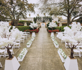 Outdoor wedding aisle with white chairs and blossom trees leads to a floral archway, perfect for a romantic Louisiana wedding.