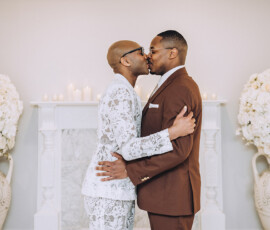 Two men kiss at their wedding in front of a flower and candle-adorned fireplace, inspired by romantic New Orleans weddings.