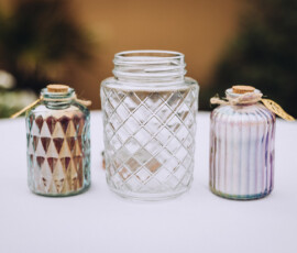 Three glass jars on white: two small layered sand jars with corks, and one larger empty jar with a diamond design.