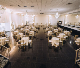 Banquet hall with round tables, gold chairs, chandeliers, glossy black floors, set for a formal event or wedding.