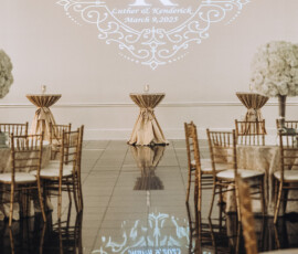 Chic wedding venue with gold chairs, tall floral centerpieces, and a monogram for Luther & Kendrick above a mirrored floor.