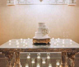White tiered wedding cake with white flowers on a marble table, lit candles, chandelier, and elegant railings in New Orleans.