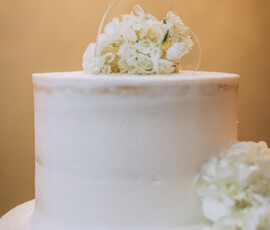 Elegant white frosted cake with minimal decor and white flowers, ideal for weddings, set against a soft neutral background.