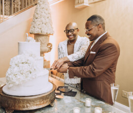 Couple cutting a white floral wedding cake in Louisiana, smiling in formal attire beside candles and champagne at the reception.