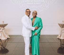 Two people in white and green suits smile arm-in-arm at their Louisiana wedding, with “Luther & Kenderick” projected behind.
