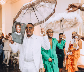A man in white leads a festive indoor parade with colorful umbrellas, inspiring vibrant Gulf South wedding celebrations.