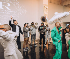 Guests dance joyfully to a brass band at a New Orleans wedding for Luther & Kendrick, March 9, 2025, with a white feathered umbrella.