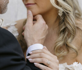 Close-up portrait of couple embracing, highlighting an engagement ring and wedding attire details.