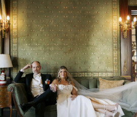 Couple relaxing together on a vintage green sofa inside an ornate historic room during wedding portraits.