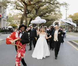 New Orleans second line wedding parade with couple walking behind a brass band and parade leader carrying a decorated umbrella.