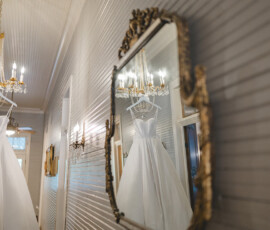 White wedding dress on chandelier reflected in ornate mirror, elegant hallway with gold fixtures, classic New Orleans wedding style.