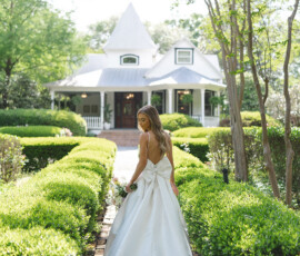 Bride in white gown on brick path with green hedges, charming house in background; romantic New Orleans wedding inspiration.