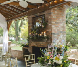 Elegant outdoor Louisiana wedding patio with gold chairs, round tables, florals, fireplace, drapes, and string lights.