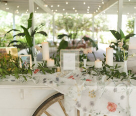 Charming Louisiana wedding table with candles, photos, greenery, and floral cloth under string lights on a covered patio.