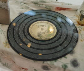Vinyl record with gold Trey & Shelby 9.19.22 label on floral tablecloth, gold candle holder; elegant Louisiana wedding.