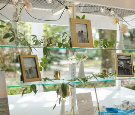 Elegant glass shelves with framed photos, greenery, and candles at a Louisiana wedding, white flowers and string lights glowing.