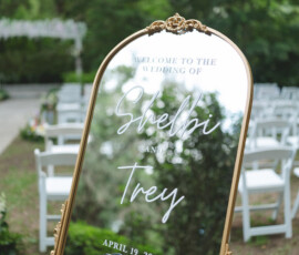 Gold mirror wedding sign for Shelbi and Trey, April 19, 2025, with white chairs and greenery outdoors in Louisiana.