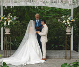 Bride and groom under a floral arch at their Louisiana outdoor wedding, facing each other as the officiant reads.