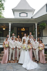 Wedding party portrait on historic home steps with bridesmaids in blush dresses and groomsmen in beige suits.
