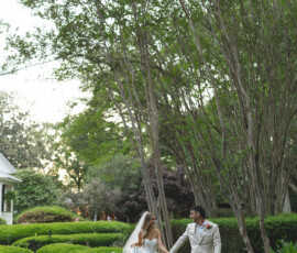Bride and groom hold hands in a lush Louisiana garden, surrounded by hedges, tall trees, and soft natural light.