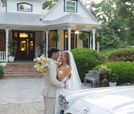 Bride and groom embrace by a vintage white Corvette in front of a charming white house, perfect for a Gulf South wedding.