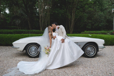 Newlyweds kissing beside a classic white vintage car during outdoor wedding portraits.