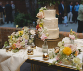 Elegant three-tiered white wedding cake with floral decor and gold accents at an outdoor New Orleans wedding reception.