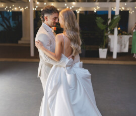 Bride and groom share a romantic first dance under string lights at their New Orleans wedding; she wears a white gown, he a light suit.