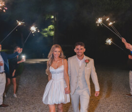 Smiling couple in wedding attire walks hand-in-hand at night, surrounded by sparklers at a joyful New Orleans wedding.