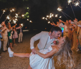 Bride in sneakers and groom in suit share a dramatic nighttime kiss, surrounded by guests with sparklers at Gulf South wedding.