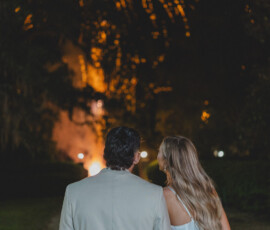 A couple in formal attire holds hands outdoors at night, watching golden fireworks—magical New Orleans wedding inspiration.