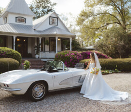 Bride in white gown by vintage convertible outside a charming house with flowers—Louisiana wedding inspiration.