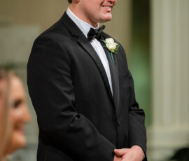 Man in black tuxedo with bow tie and boutonniere smiles indoors, reflecting classic Louisiana wedding elegance.