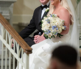 Bride in white dress and veil with bouquet sits by groom in black tuxedo, smiling in romantic New Orleans church wedding.