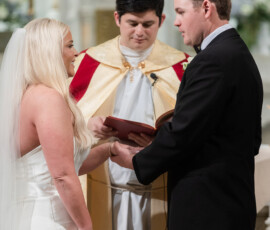 Bride and groom exchange vows at the altar with a priest in ceremonial robes in a classic New Orleans church wedding.