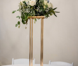 Gold centerpiece with white and blue flowers, greenery, and roses on a round table with votive candles and a Reserved sign.