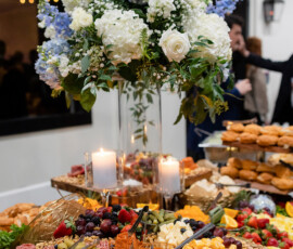Elegant grazing table with cheeses, fruits, meats, and candles beneath white and blue flowers—ideal for a Louisiana wedding.