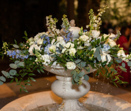 White stone fountain with white and blue flowers, green leaves, and flowing water at a Louisiana wedding.